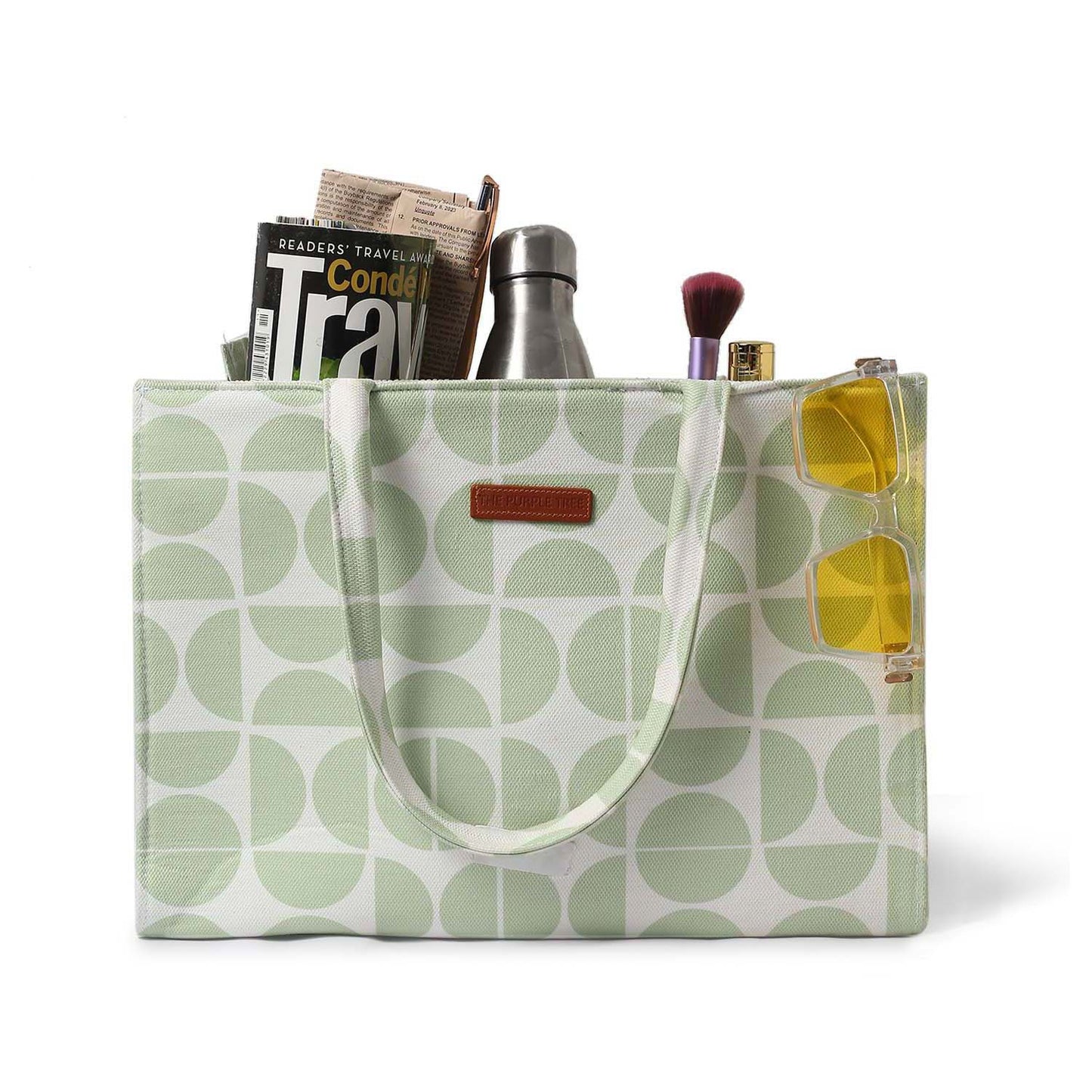 Green and white tote bag with book and notebook on wooden table.
