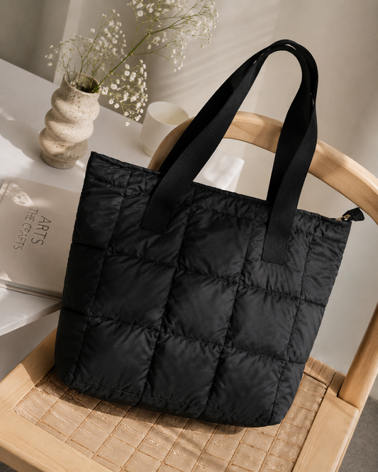 Black puffer tote bag on a wooden chair with a minimal background
