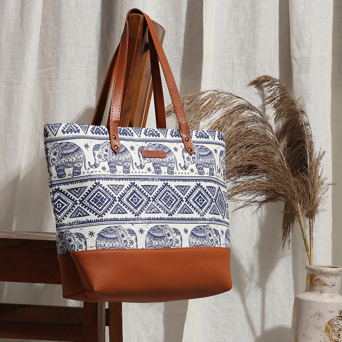 An elegant leather tote bag with an elephant print design. It features a sturdy brown handle for easy carrying.