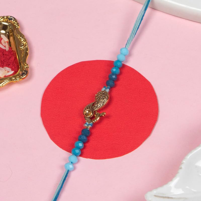 On the table, a peacock charm rests on a rakhi beside a bowl of red powder, adding a touch of tradition and color.