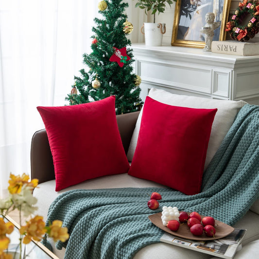A cozy couch adorned with two red pillows sits next to a vibrant Christmas tree, enhancing the holiday spirit.