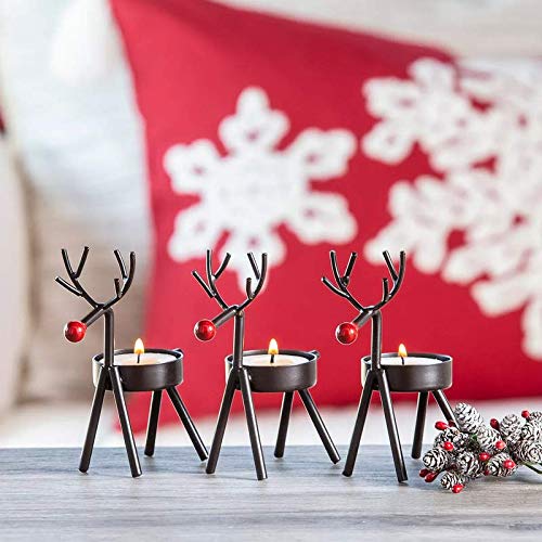 Three black reindeer candles on a table with a red pillow.