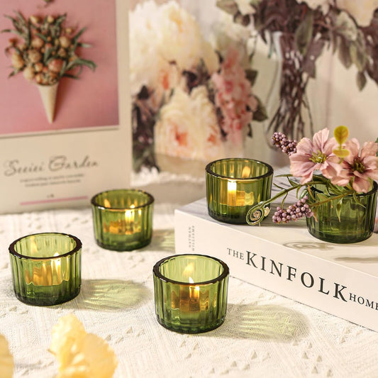 Green glass candle holders with lit candles on a surface with decorative elements.