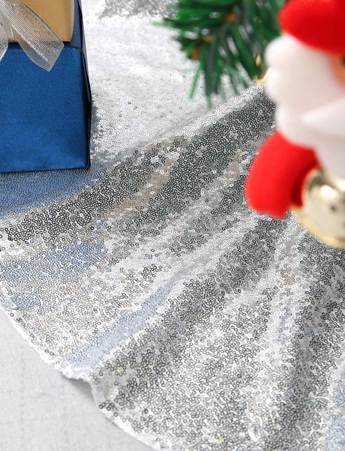 Close-up of a glittery surface with a Santa Claus figurine and blue box in the background.