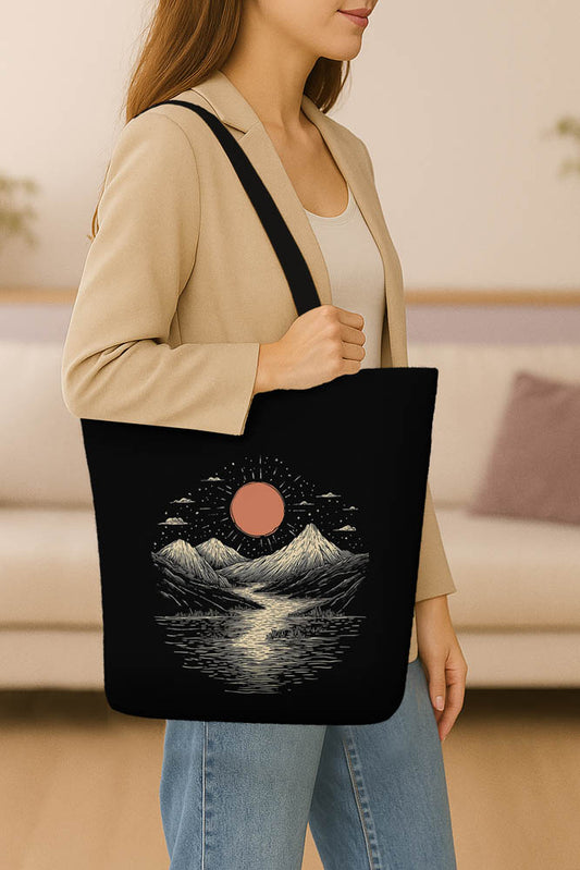 A black tote bag adorned with a mountain scene and sun, representing a tranquil nature theme.
