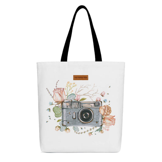 A white tote bag featuring a photo of a camera surrounded by colorful flowers.