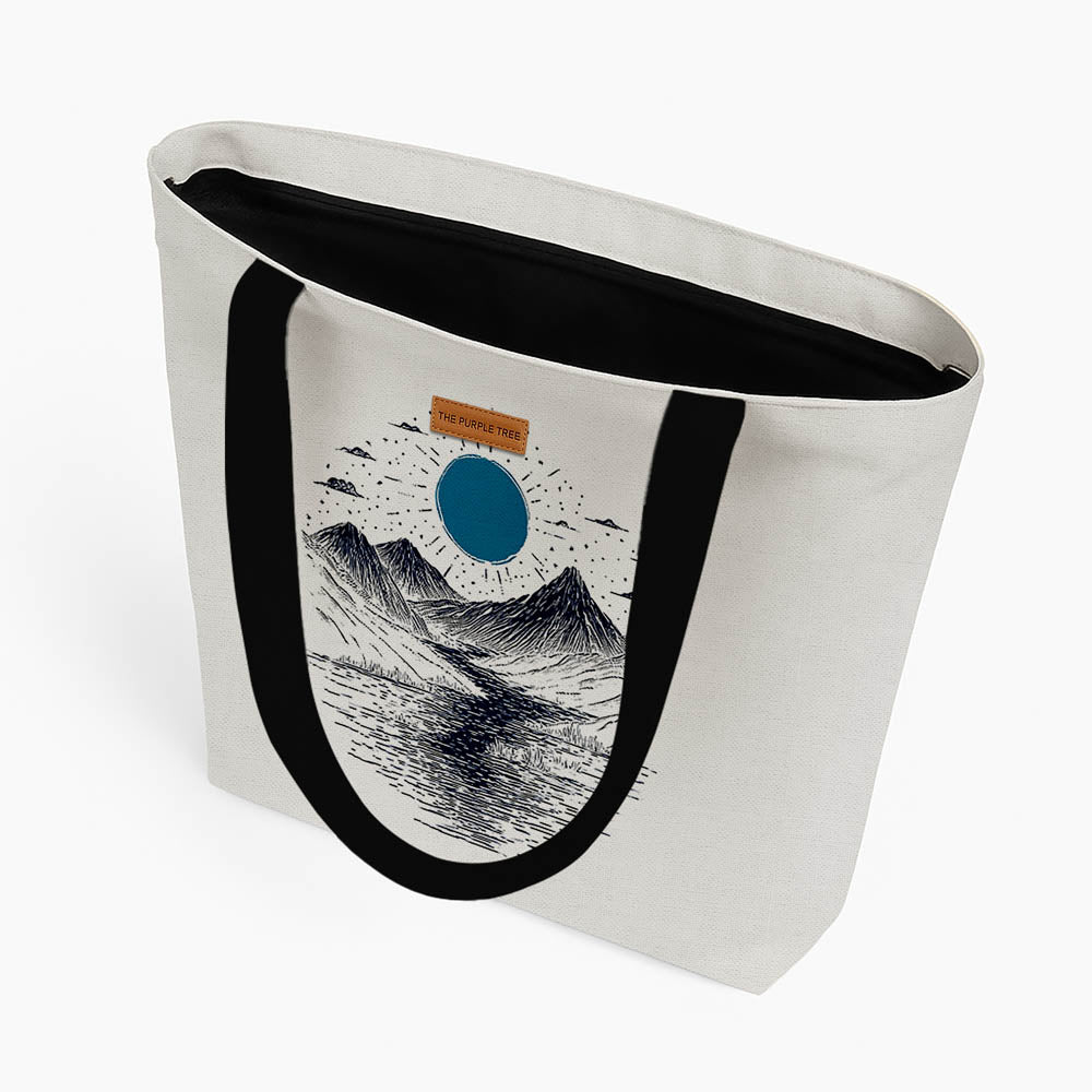 A tote bag showcasing a picturesque mountain view with a luminous blue moon overhead.