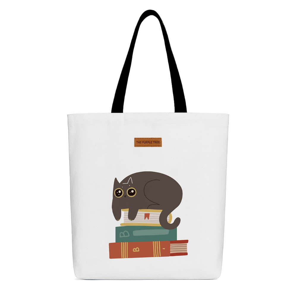 A tote bag featuring a cat perched on a stack of colorful books, showcasing a cozy reading theme.