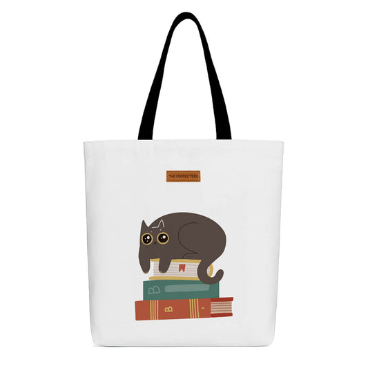 A tote bag featuring a cat perched on a stack of colorful books, showcasing a cozy reading theme.