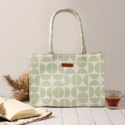 Green and white tote bag with book and notebook on wooden table.