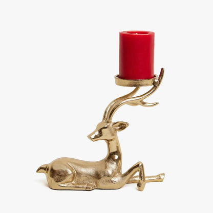 Gold deer-shaped candle holder with a lit candle on a wooden surface, Christmas tree and decorations in the background.