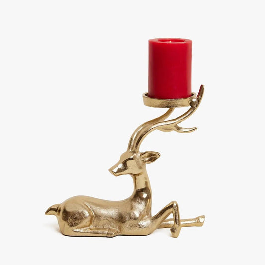Gold deer-shaped candle holder with a lit candle on a wooden surface, Christmas tree and decorations in the background.