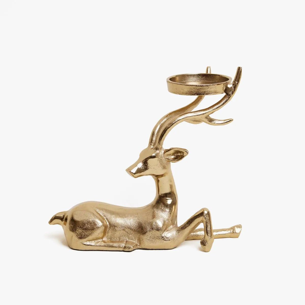 Gold deer-shaped candle holder with a lit candle on a wooden surface, Christmas tree and decorations in the background.