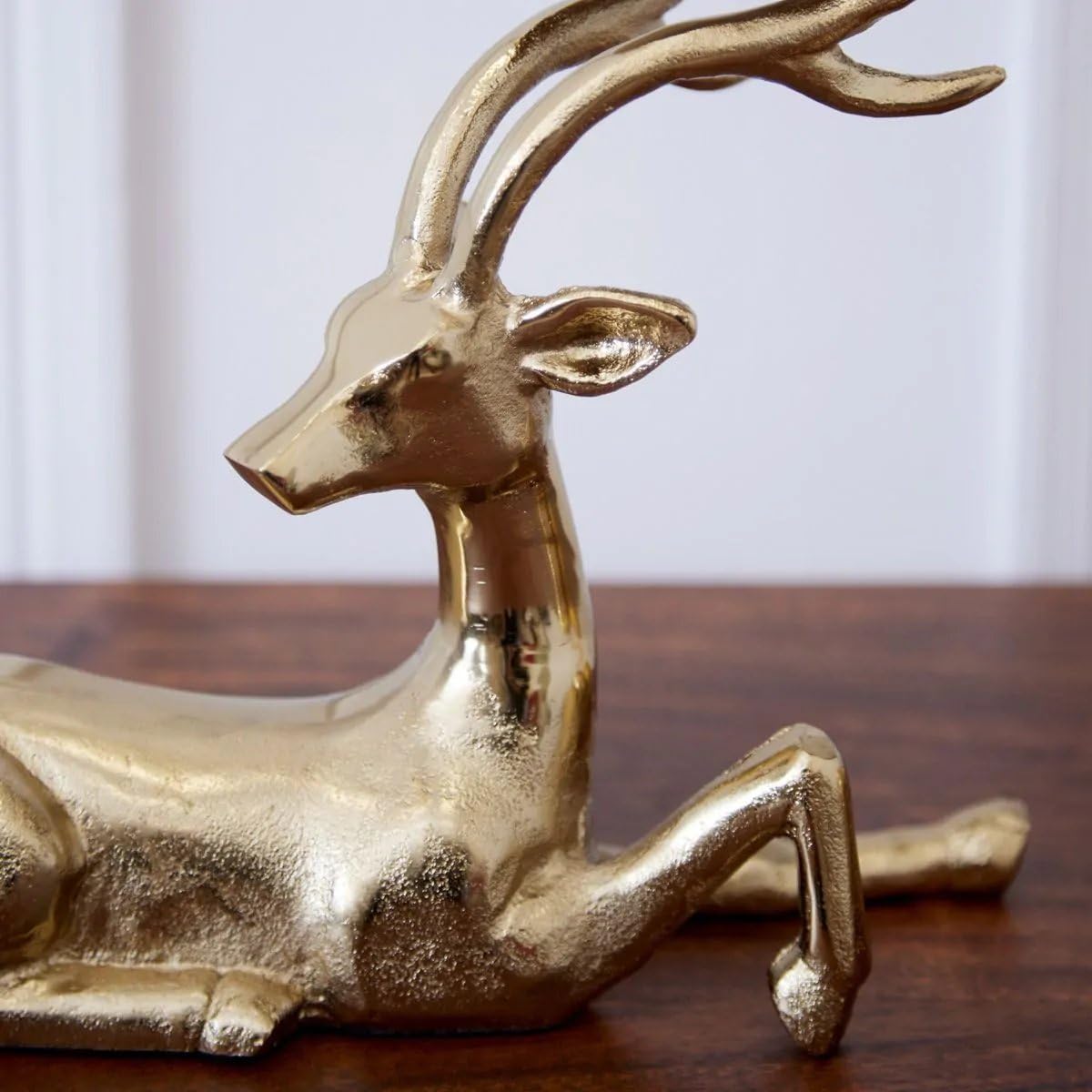 Gold deer-shaped candle holder with a lit candle on a wooden surface, Christmas tree and decorations in the background.