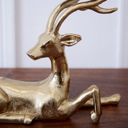 Gold deer-shaped candle holder with a lit candle on a wooden surface, Christmas tree and decorations in the background.
