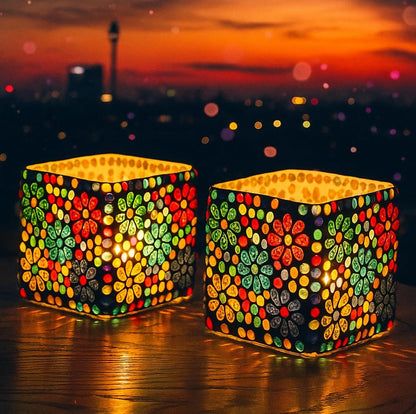 Two colorful mosaic lanterns on a reflective surface with a sunset cityscape in the background.