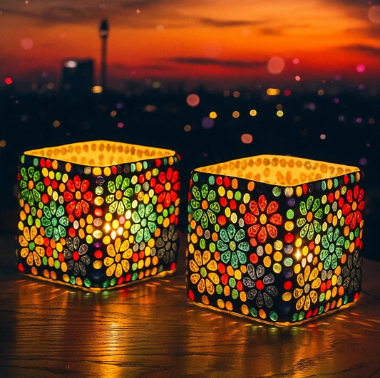 Two colorful mosaic lanterns on a reflective surface with a sunset cityscape in the background.