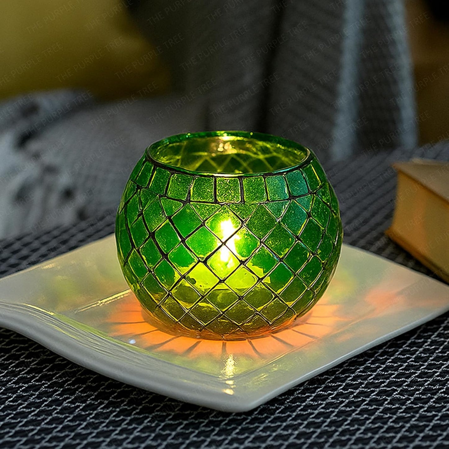 Green mosaic candle holder on a white plate with a blurred background