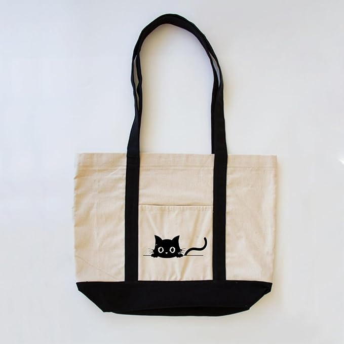  A black cat sits prominently on the front of a white tote bag, showcasing its sleek fur against the light background.