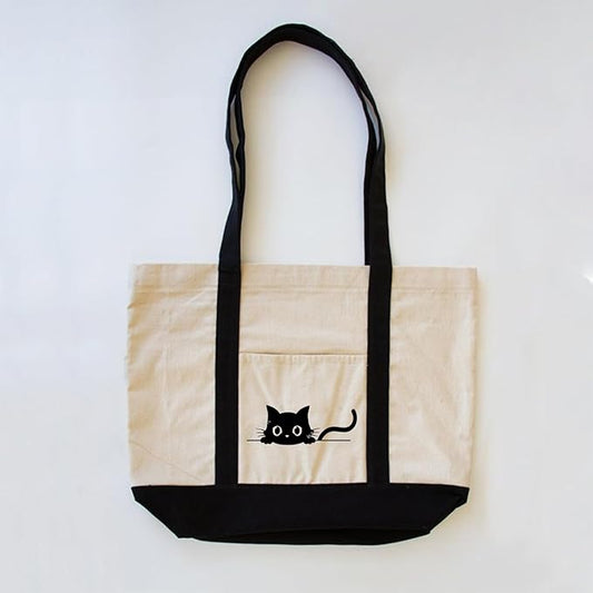  A black cat sits prominently on the front of a white tote bag, showcasing its sleek fur against the light background.