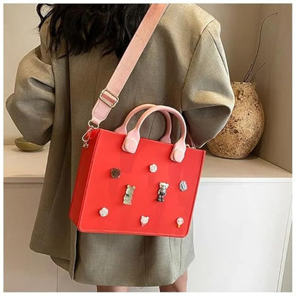 Red handbag with pink accents and decorative elements held by a person wearing a green coat.