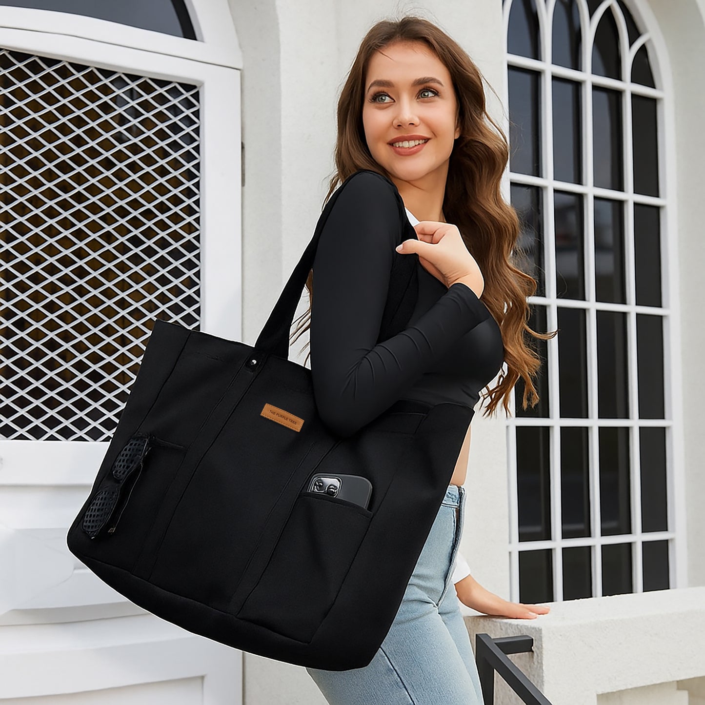 Woman holding a black tote bag in front of a white building with arched windows.