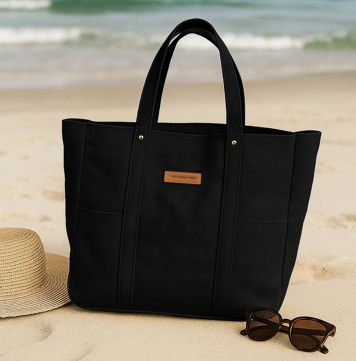 Black tote bag on a sandy beach with sunglasses and a hat nearby