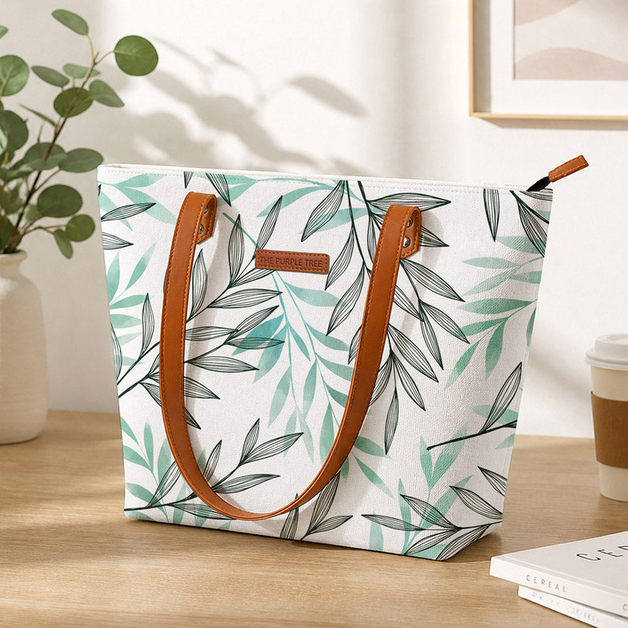 Tote bag with leaf pattern on a wooden surface with a plant and coffee cup in the background
