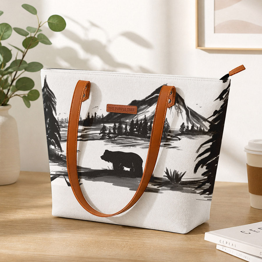 Tote bag with bear and mountain design on a wooden surface with a plant and coffee cup in the background.