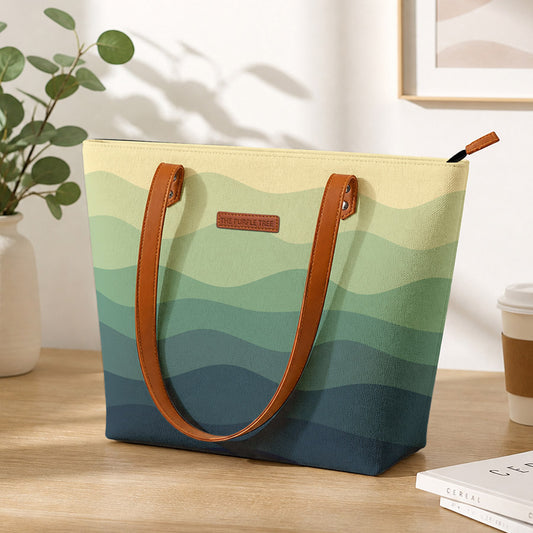 Tote bag with green and blue wave pattern on a wooden surface with a plant and coffee cup in the background.