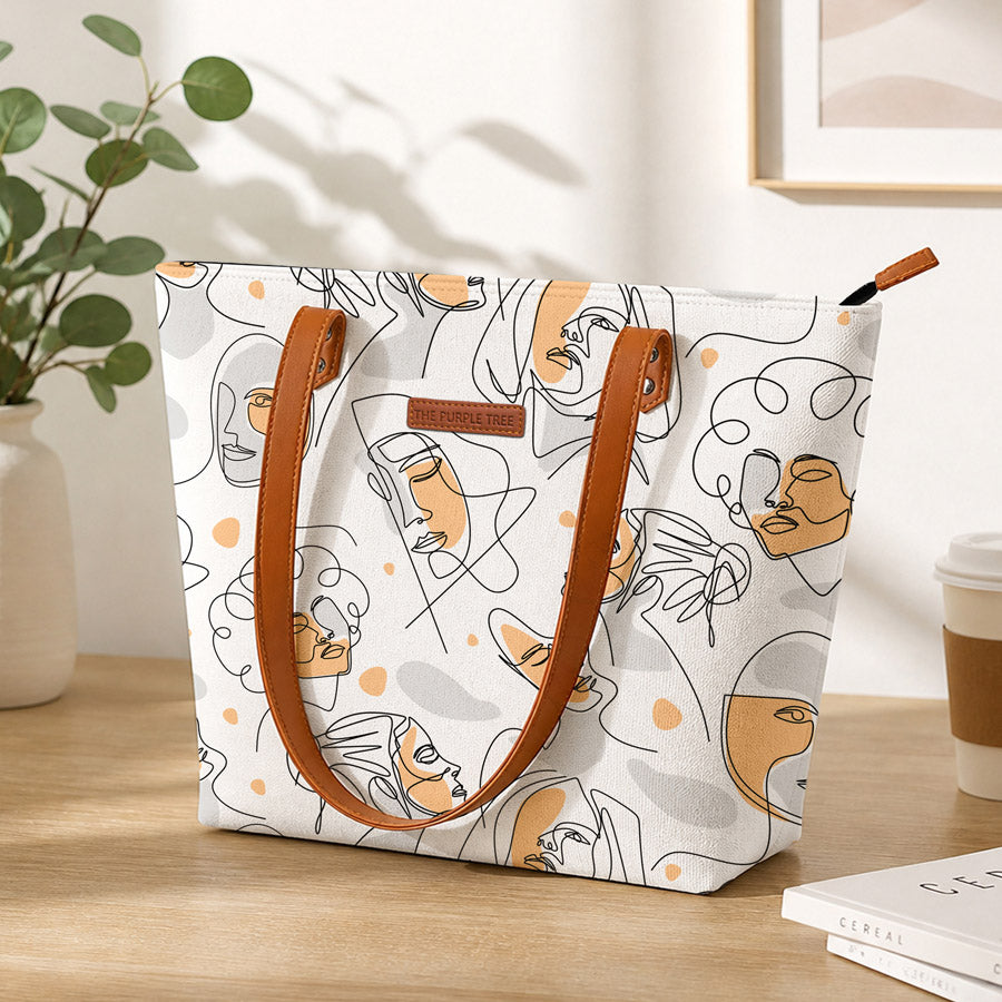 Tote bag with abstract face design on a wooden surface with a plant and coffee cup in the background