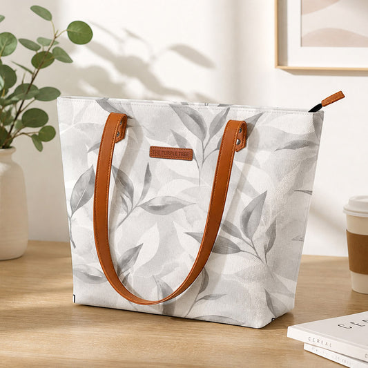 White tote bag with leaf pattern and brown handles on a wooden surface.
