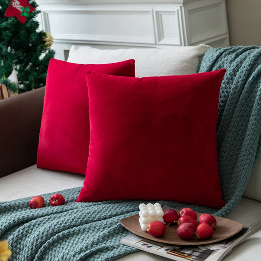 Two red pillows rest on a couch beside a beautifully decorated Christmas tree, creating a festive atmosphere.

