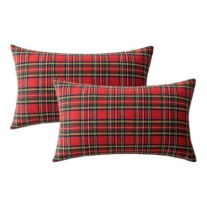  A couch adorned with two red plaid pillows sits next to a festive Christmas tree, creating a warm holiday atmosphere.
