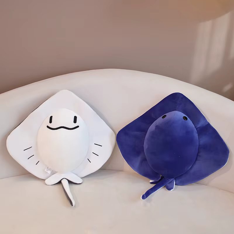 Two Sting ray plush toys, one white and one blue, on a light-colored surface.