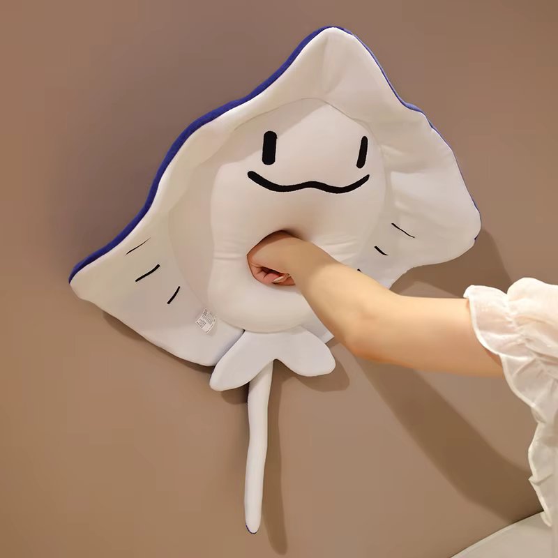 Hand holding a Sting ray-shaped pillow against a plain background