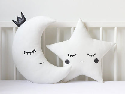 Two white and blue star-shaped pillows and a moon-shaped pillow on a bed.