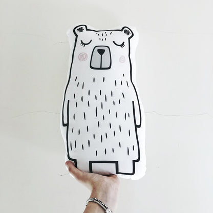 A hand holding a bear pillow against a white background.