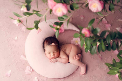 A peaceful newborn girl sleeping on a pink pillow, embraced by delicate pink flowers.