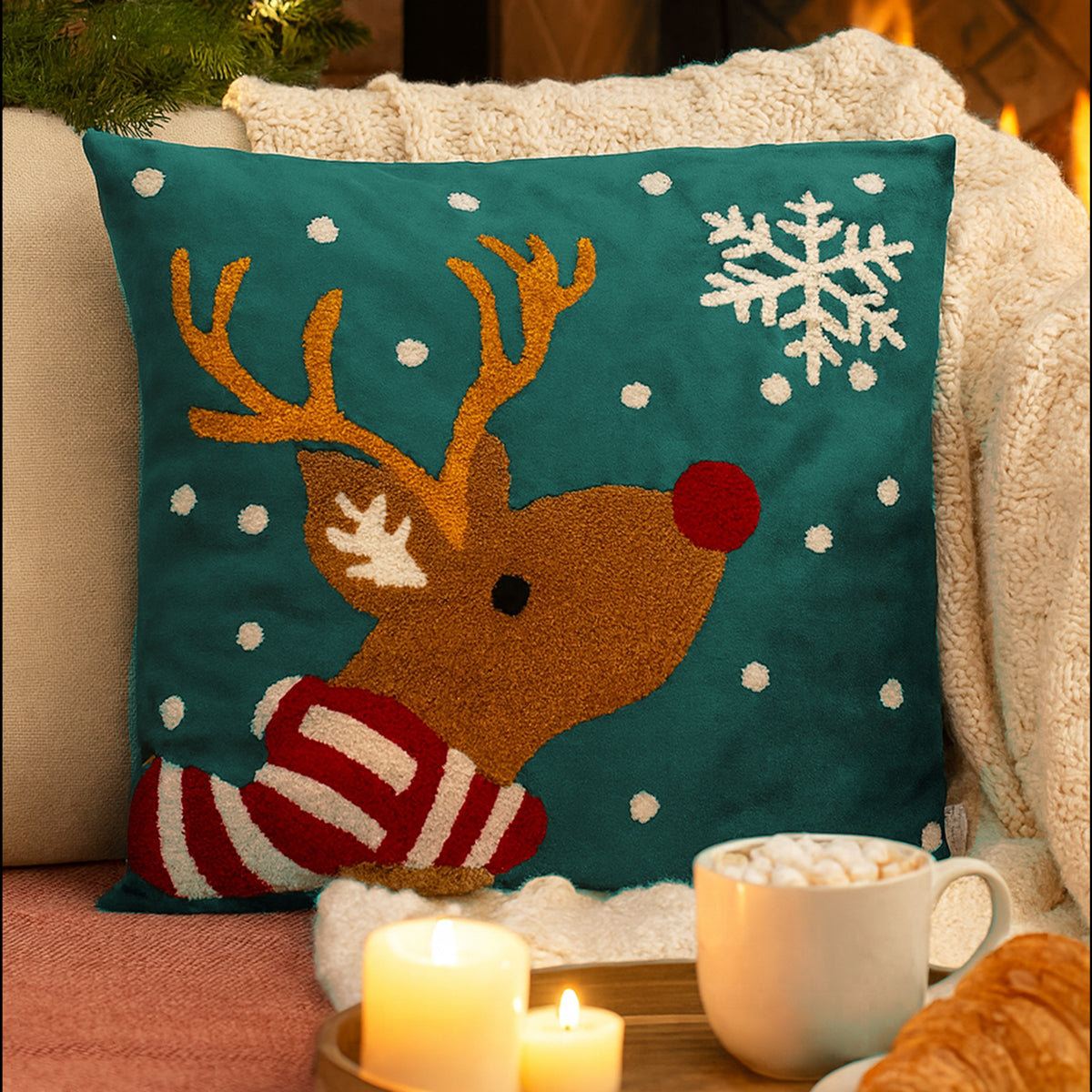 Decorative pillow with a reindeer design on a couch with candles and a mug of hot chocolate.