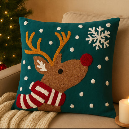 Decorative pillow with a reindeer in snow design on a couch next to a Christmas tree.