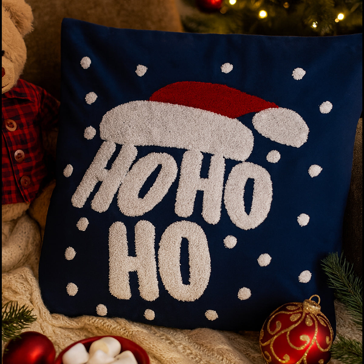 Decorative pillow with 'HO HO HO' text and Santa hat design, surrounded by Christmas decor.