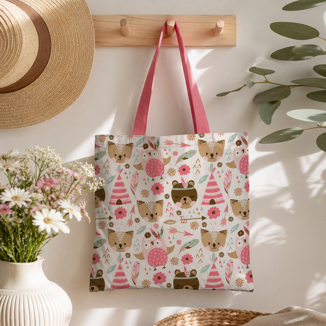 Tote bag with bear and flower pattern hanging on a hook with a hat and plant in the background