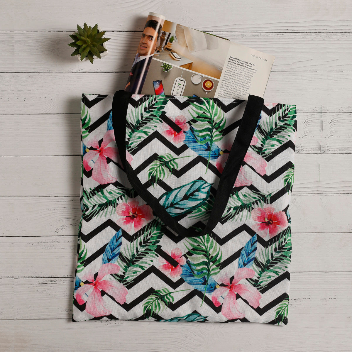 A stylish tote bag adorned with a tropical pattern and elegant black handles.