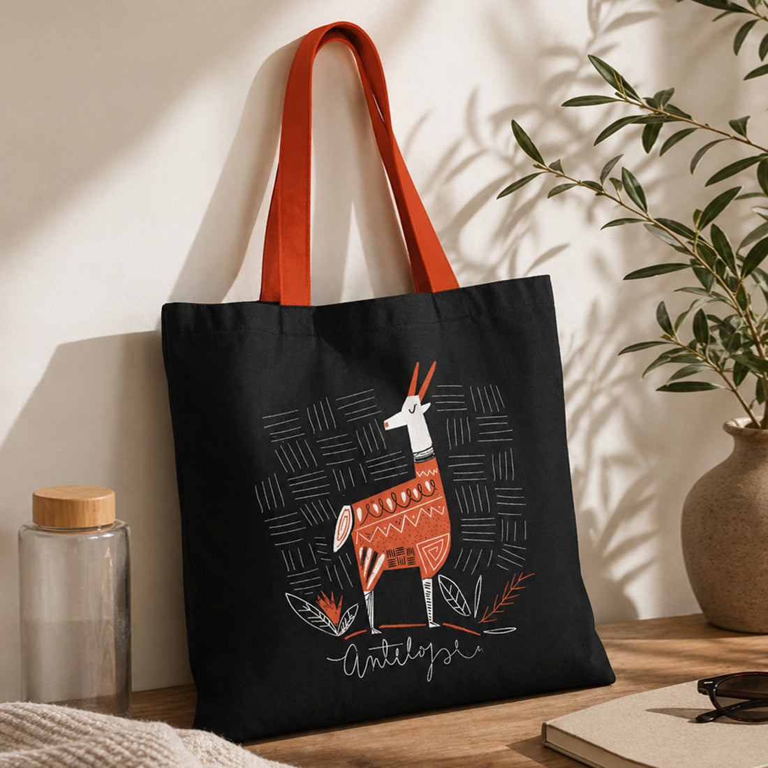 Black tote bag with a llama design on a wooden surface with a plant in the background
