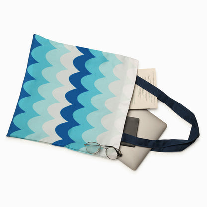A tote bag with a blue wavy pattern, containing books, a phone, and a pair of glasses.
