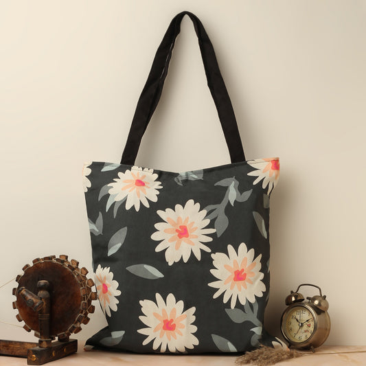 A black tote bag with a floral print design, placed next to an old-fashioned spinning wheel and a vintage alarm clock.
