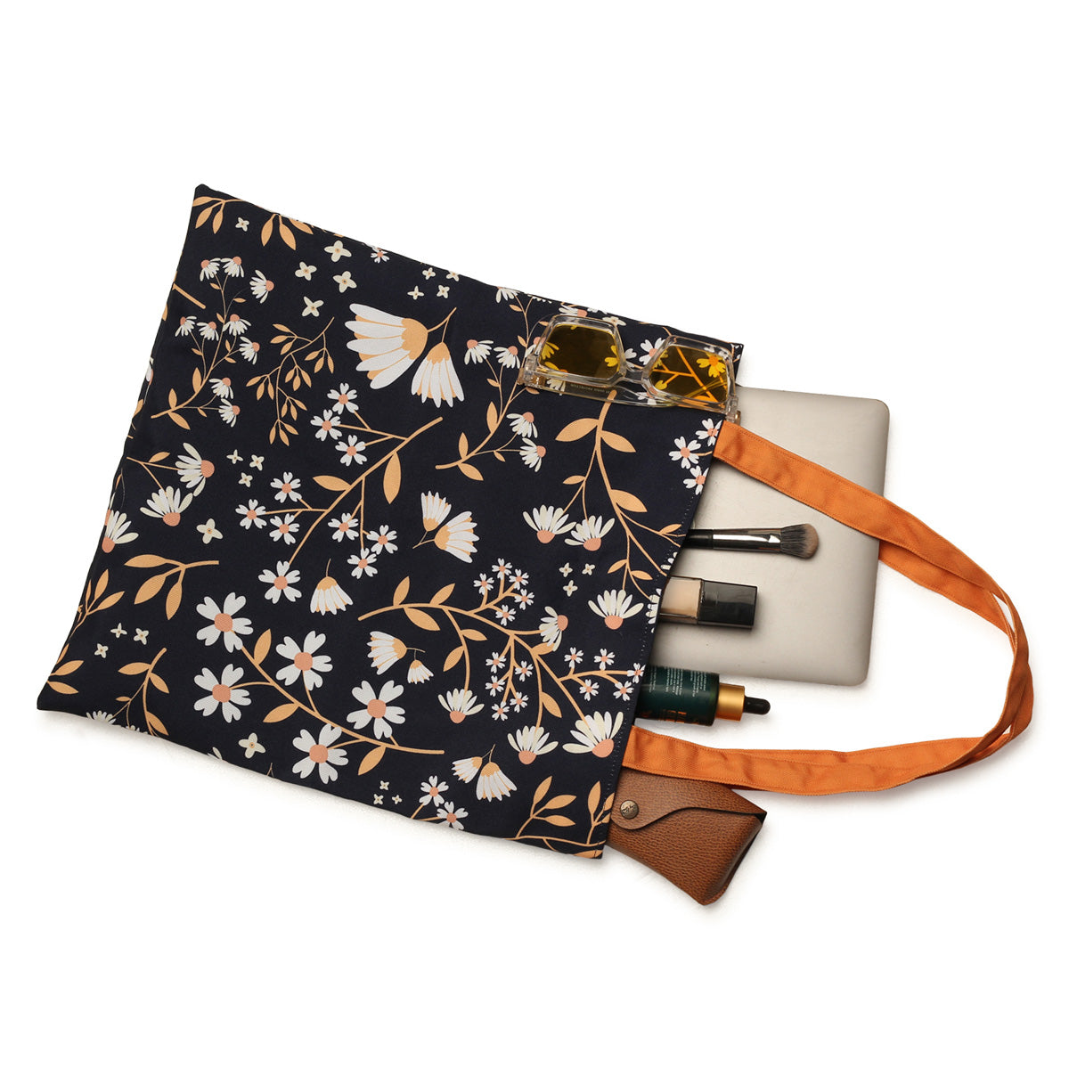 A tote bag with a floral pattern on a white background, containing a laptop, sunglasses, and cosmetic items.