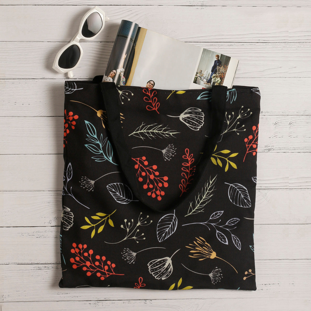 A black tote bag adorned with vibrant leaves and flowers, adding a pop of color to its elegant design.