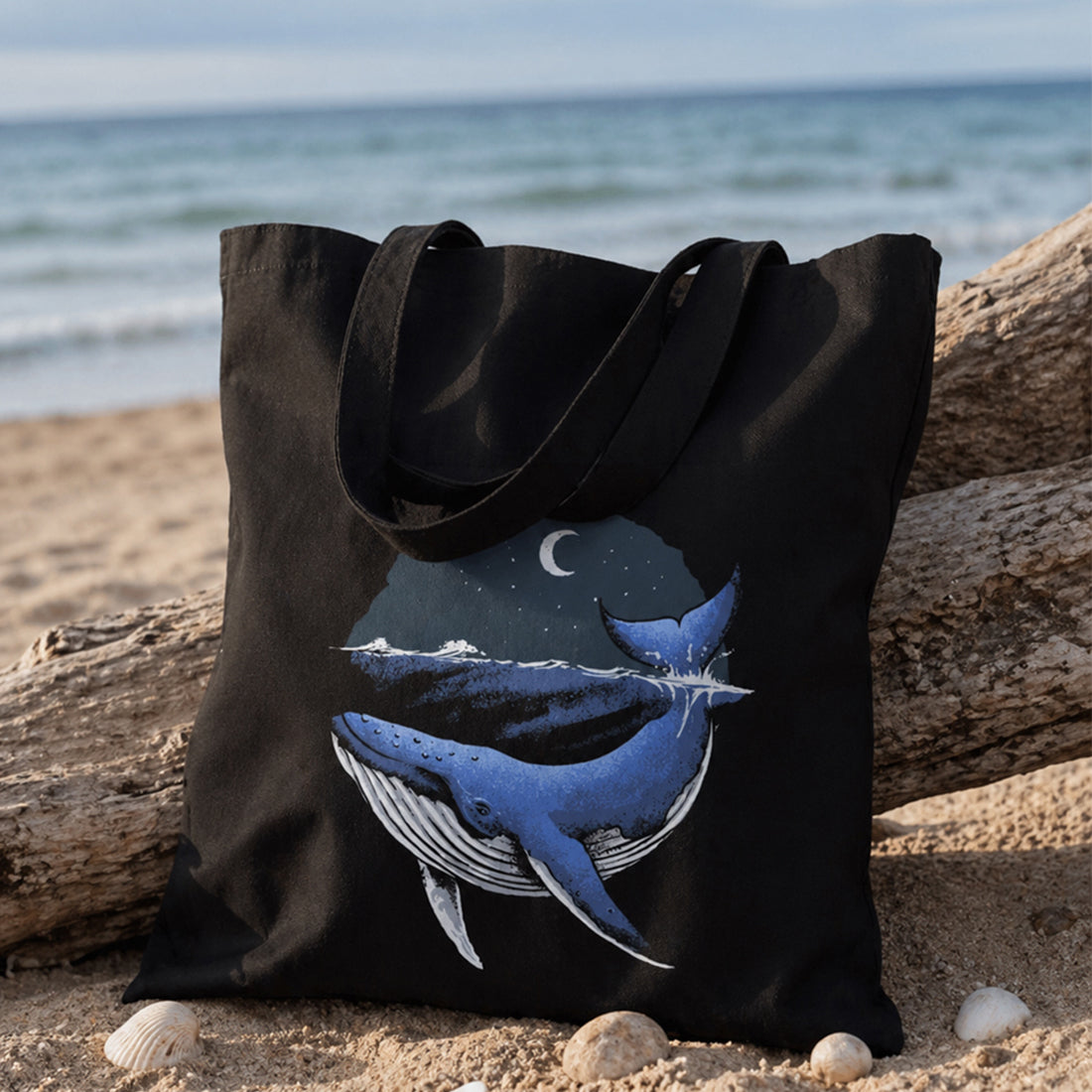 Black tote bag with whale design on a beach